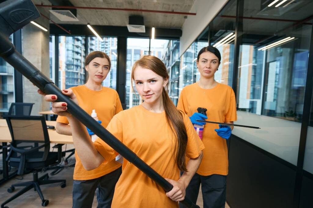Three commercial cleaning service workers pose with their tools and chemicals.