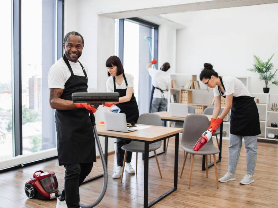 Janitorial team in white shirts underneath black aprons performs office cleaning as part of preventive building maintenance