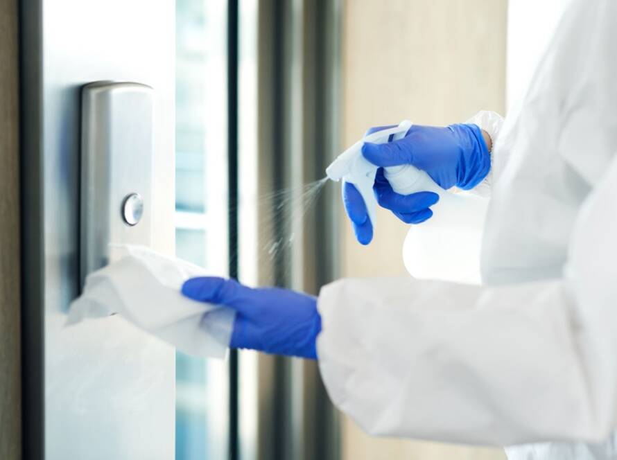 Close-up of a day porter’s hand spraying disinfectant onto a cleaning rag before wiping an elevator button for hygiene and safety