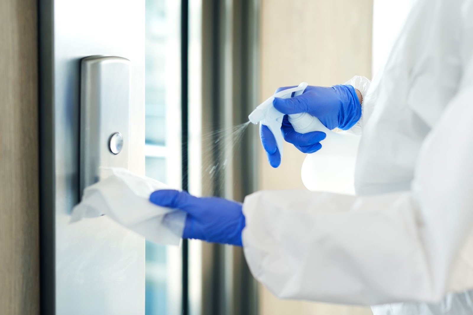 Close-up of a day porter’s hand spraying disinfectant onto a cleaning rag before wiping an elevator button for hygiene and safety