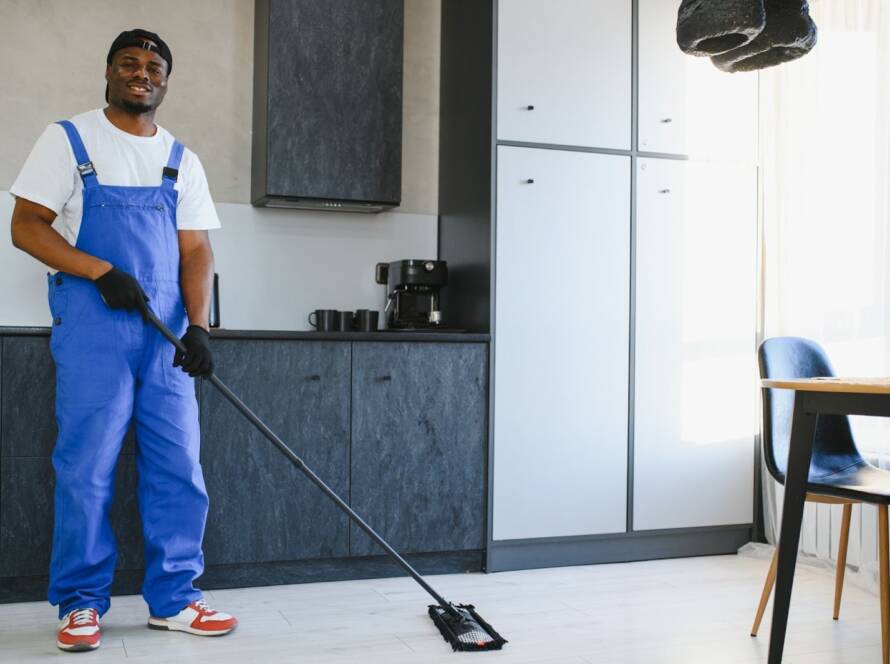 Professional male cleaner with a mop next to a table and cabinetry.