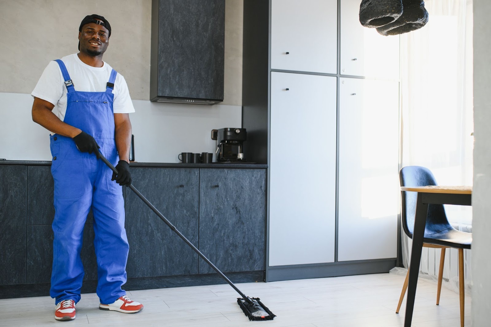 Professional male cleaner with a mop next to a table and cabinetry.