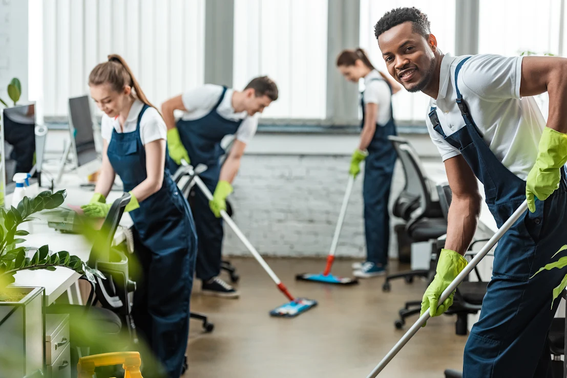 A man and his team of commercial cleaners smile as they clean an office.