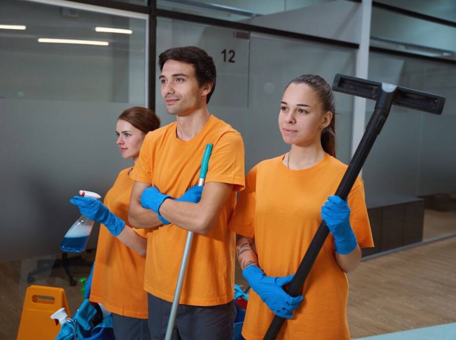 A team of professional cleaners stand in an office with their cleaning materials.