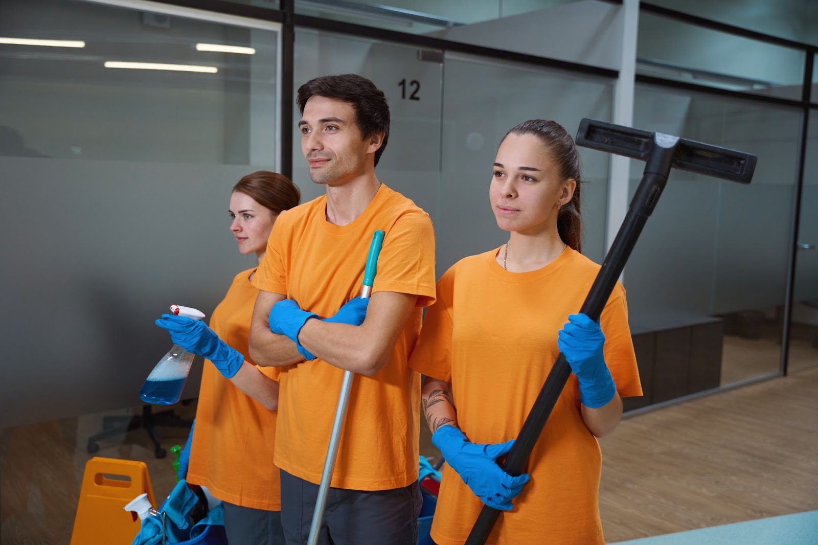 A team of professional cleaners stand in an office with their cleaning materials.