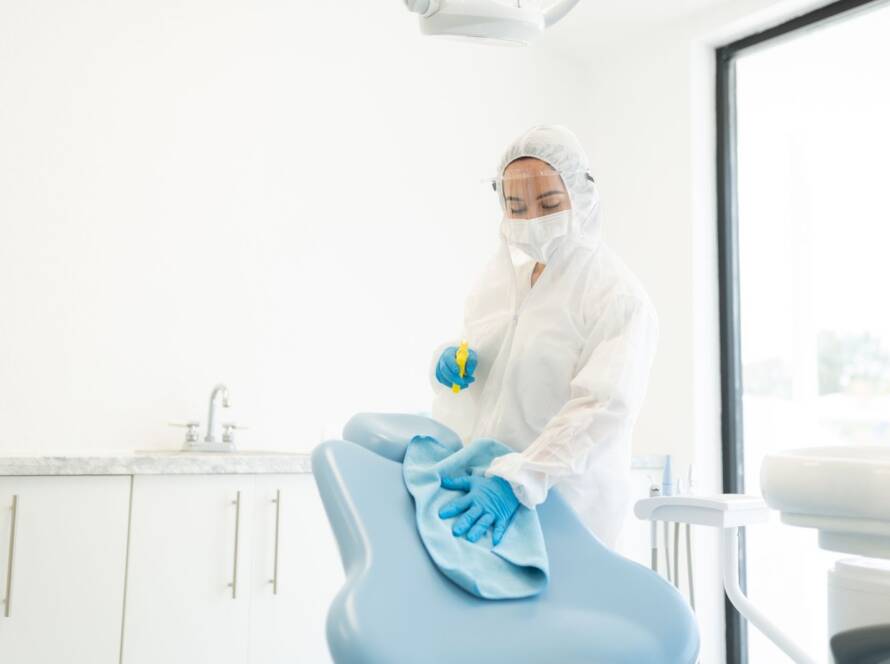 A professional cleaning service worker cleans a patient seating area in an office.