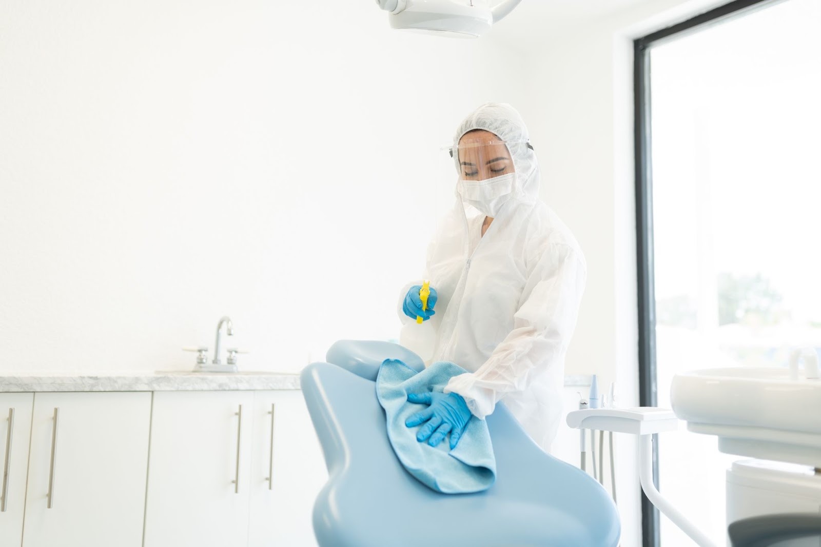 A professional cleaning service worker cleans a patient seating area in an office.
