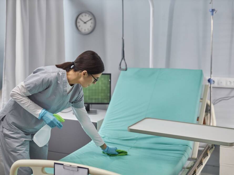 A professional medical cleaner sanitizes a patient bed.