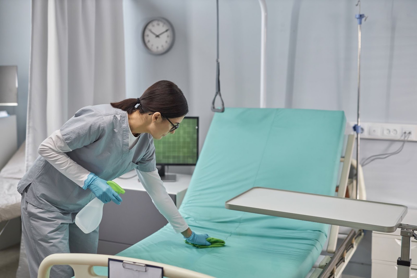 A professional medical cleaner sanitizes a patient bed.