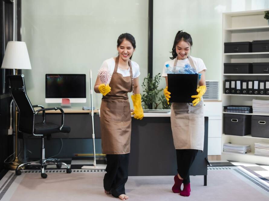 Two gloved cleaners smile as they clean an office.