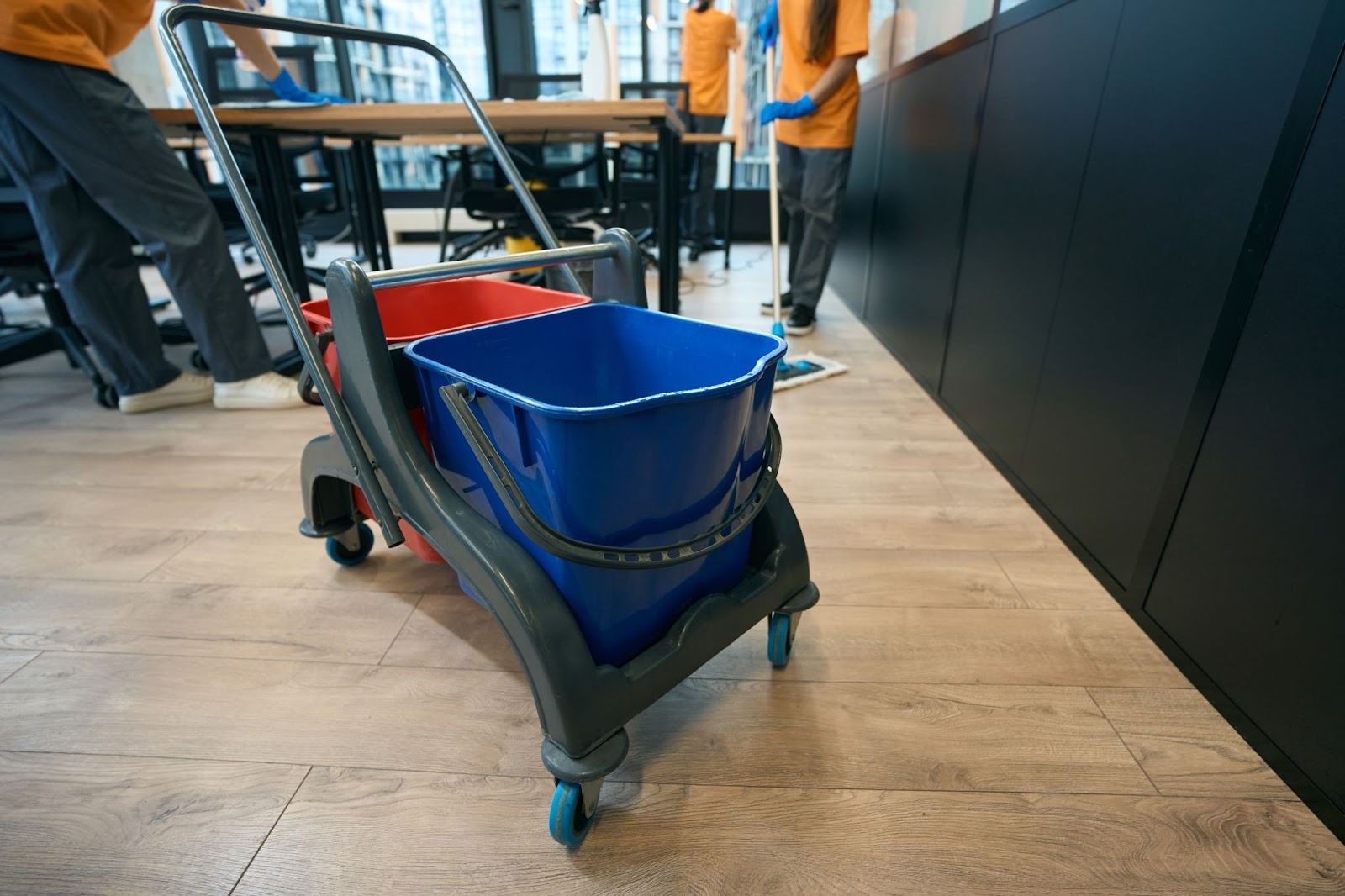 Janitorial cleaning service crew cleaning a coworking area floor, with a cleaning bucket in the foreground.